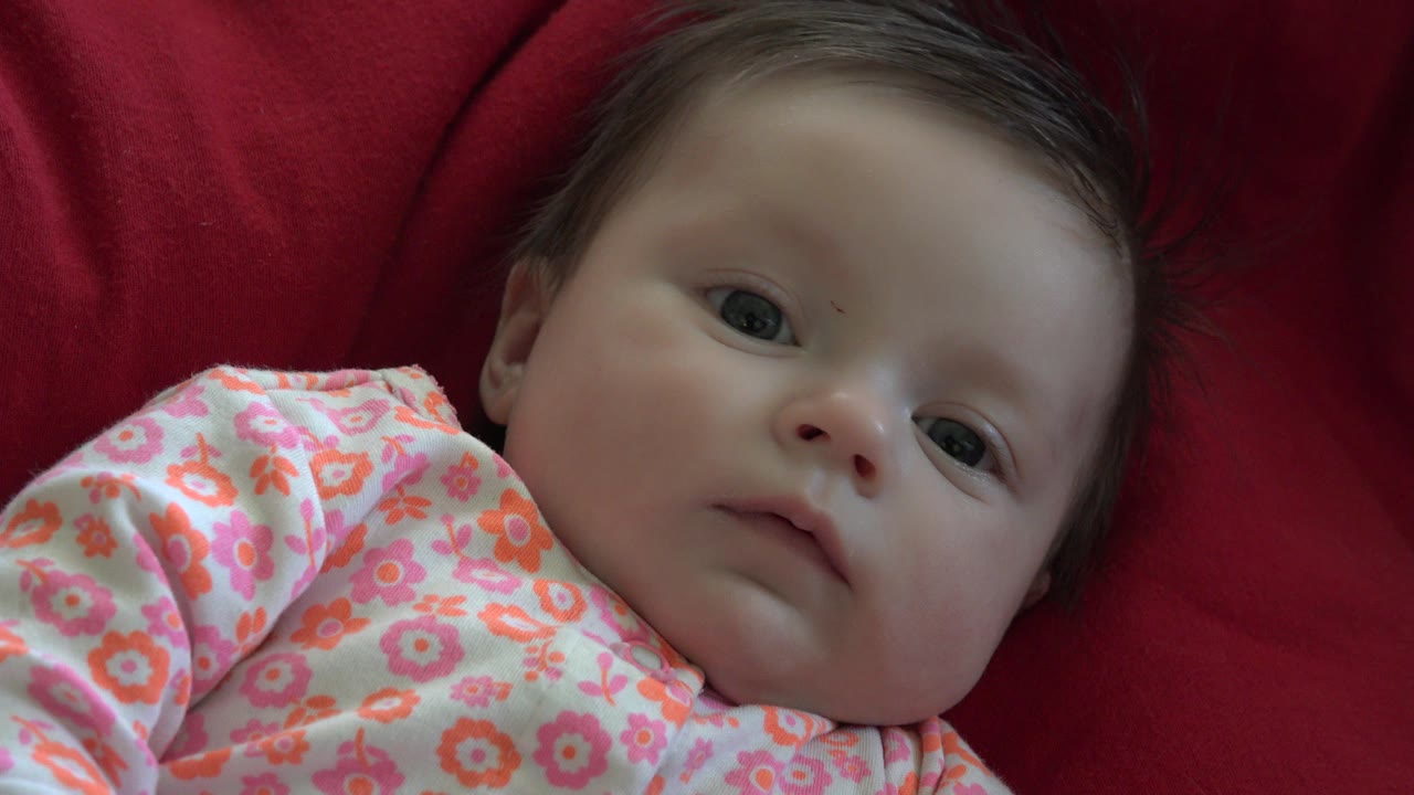 At 0:01, the baby's face remains centered near the lens, with the pink patterned clothing visible across the lower frame in Westminster, Colorado.