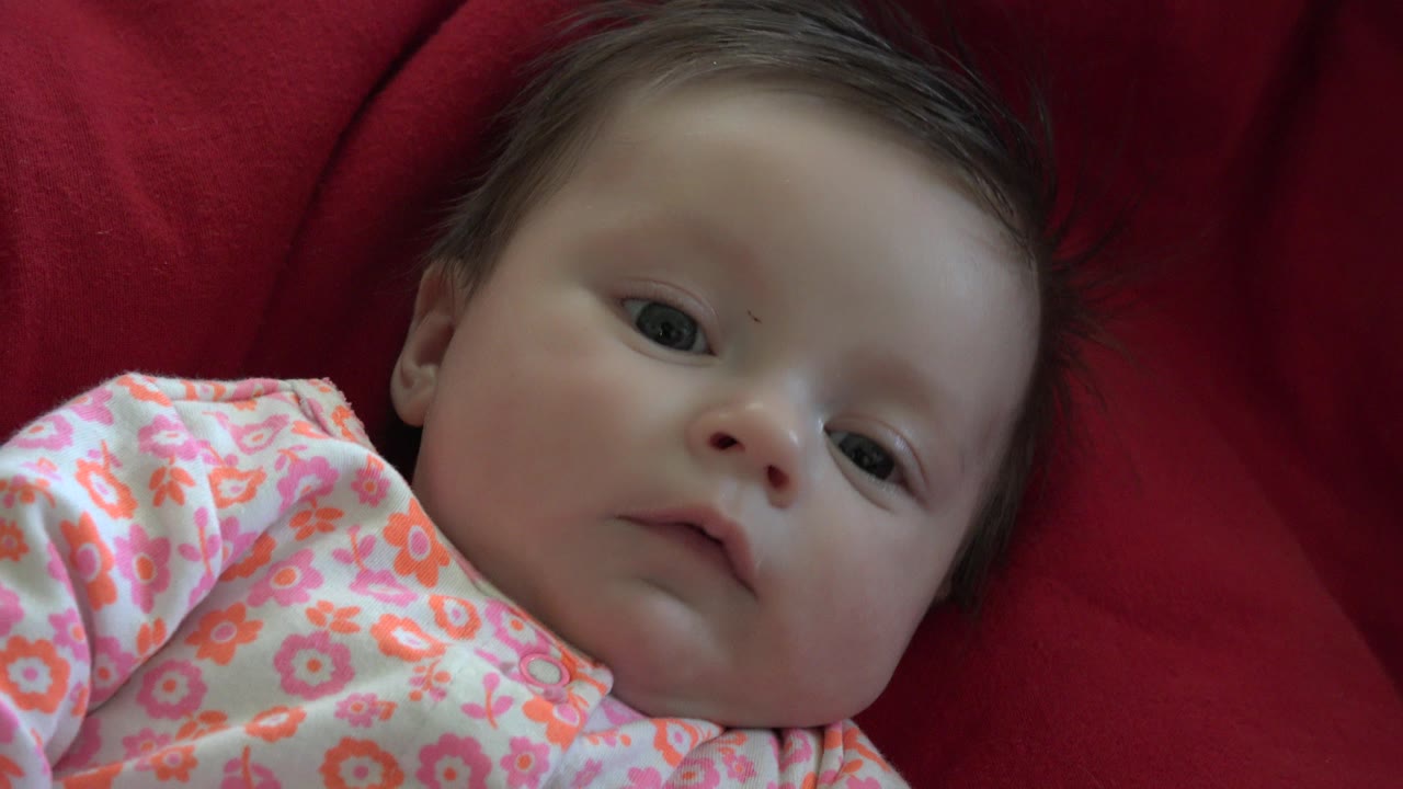 Baby in a floral sleeper lying on a red blanket.
