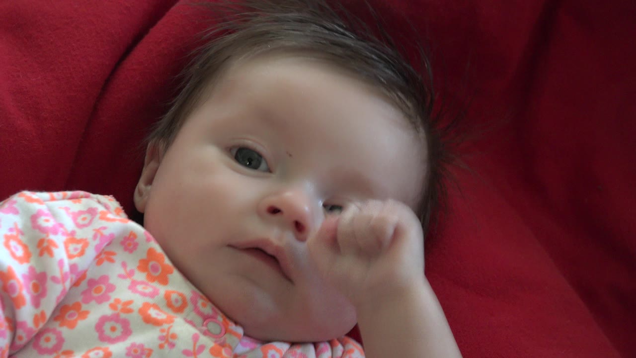 Baby lying on a red blanket with one fist raised near the face.
