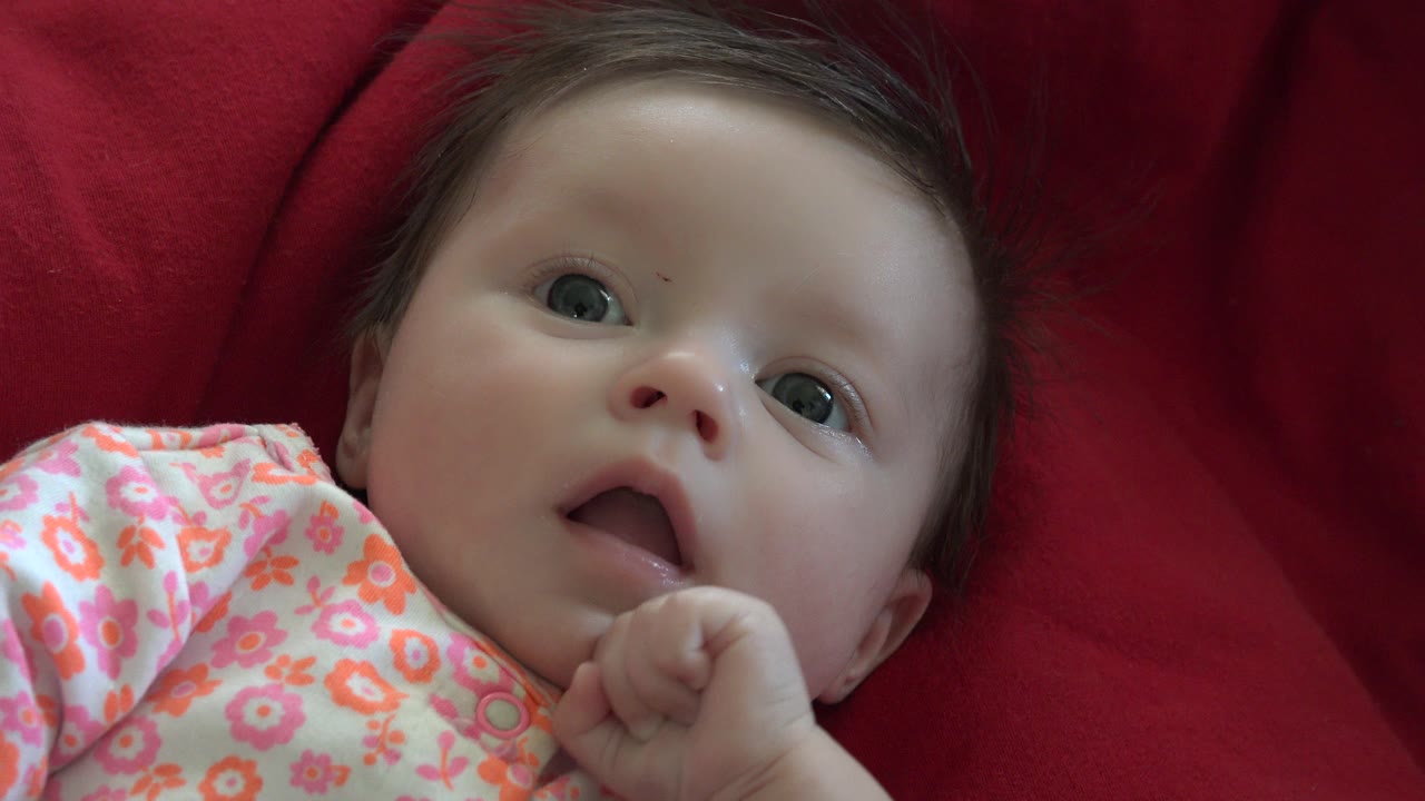 Baby lying on a red quilted blanket in a floral romper.