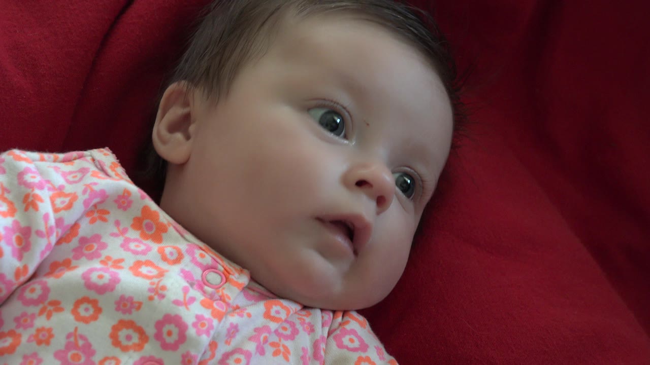 Close-up of a baby in Westminster, Colorado lying on deep red fabric, looking off to the side in a pink floral outfit.