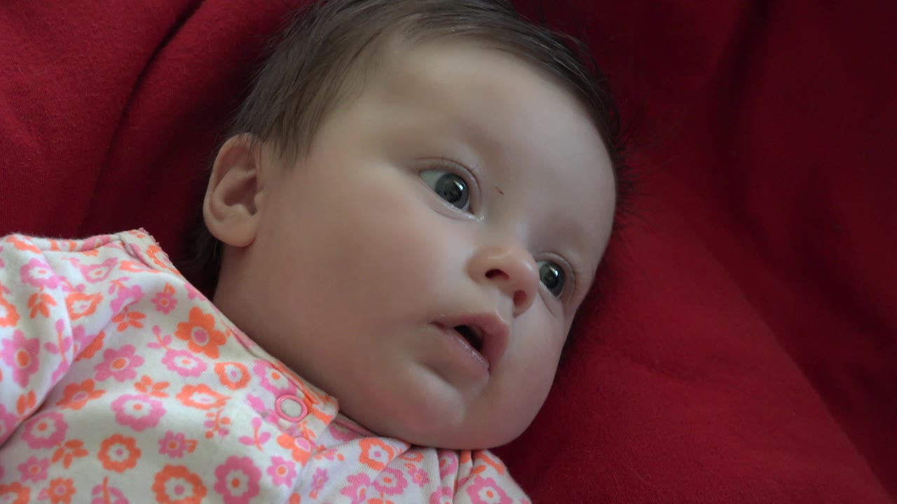 Baby looking upward from a red fabric surface.
