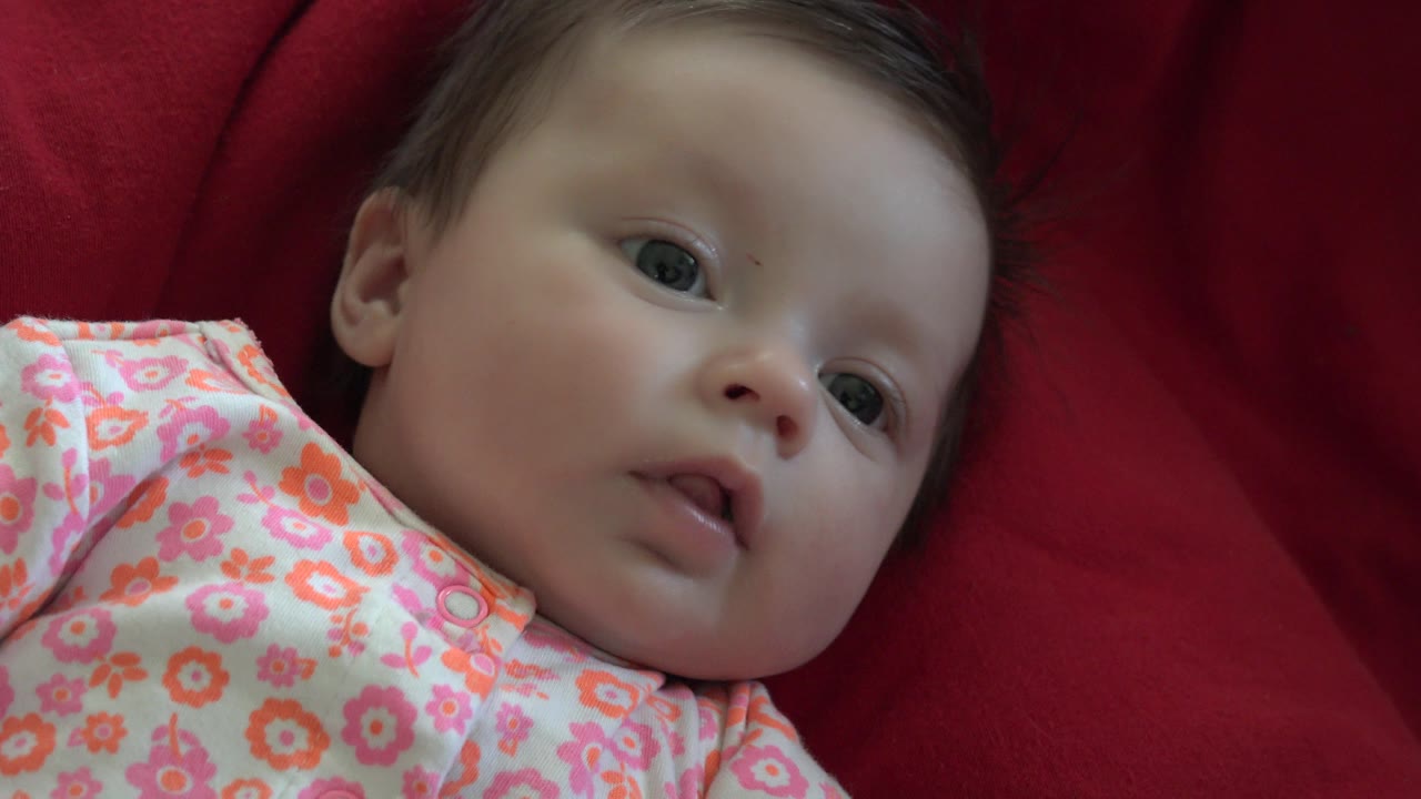Baby looking upward from a red fabric surface.