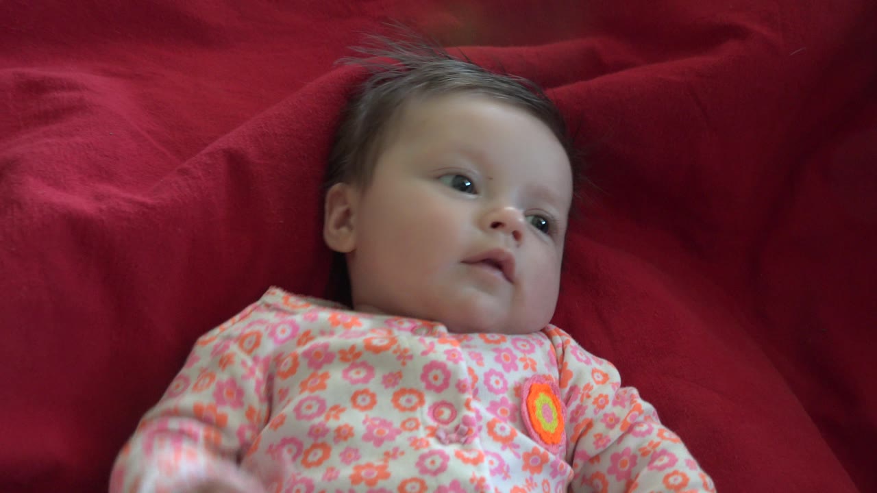 Baby on red blanket looking off to the side.