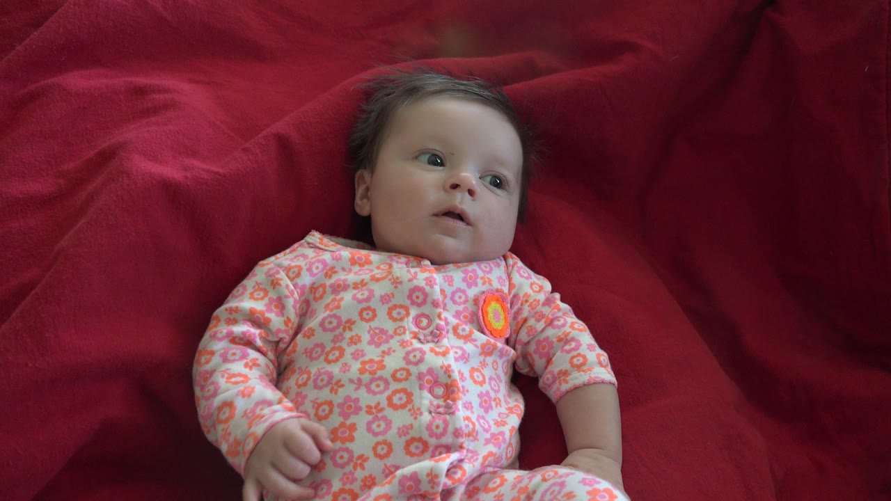 The baby remains on the red blanket in Westminster, Colorado, with eyes open and one hand resting near the body.