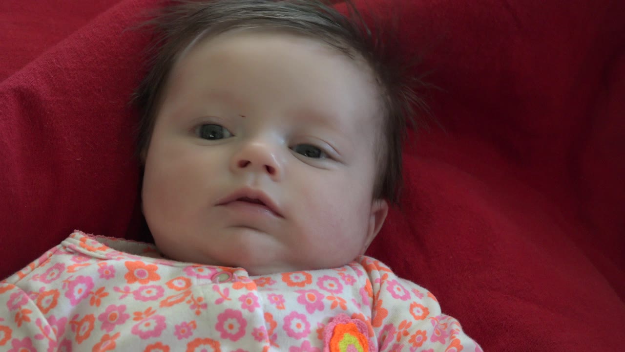 Baby lying on a red blanket in a floral outfit.