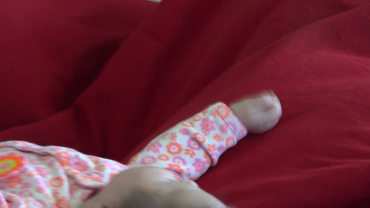 Baby in floral clothing lying on a red cushion.