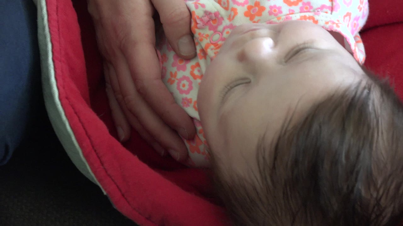 Baby girl lying on a red blanket as adult hands rest near her side.