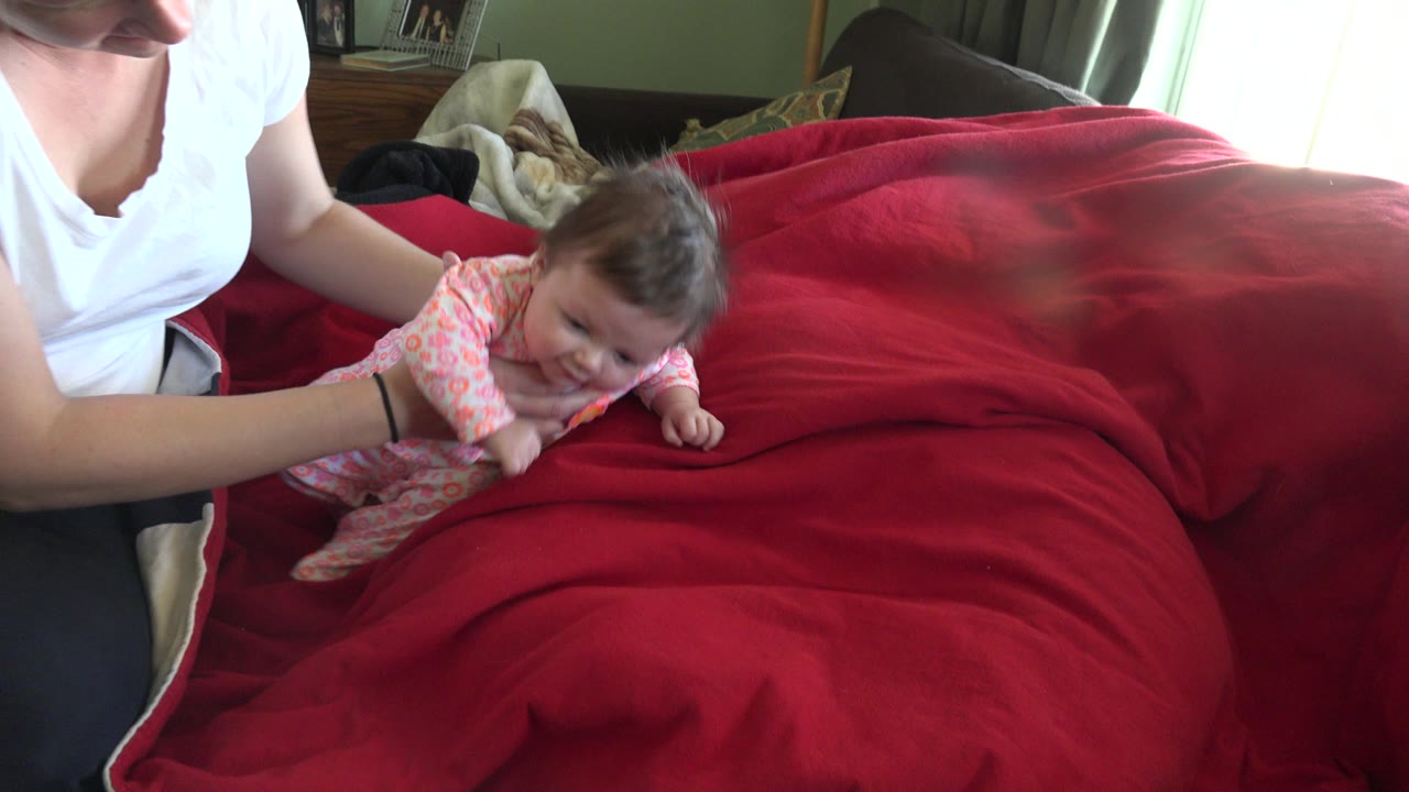 Adult supports a baby lying on a red blanket.
