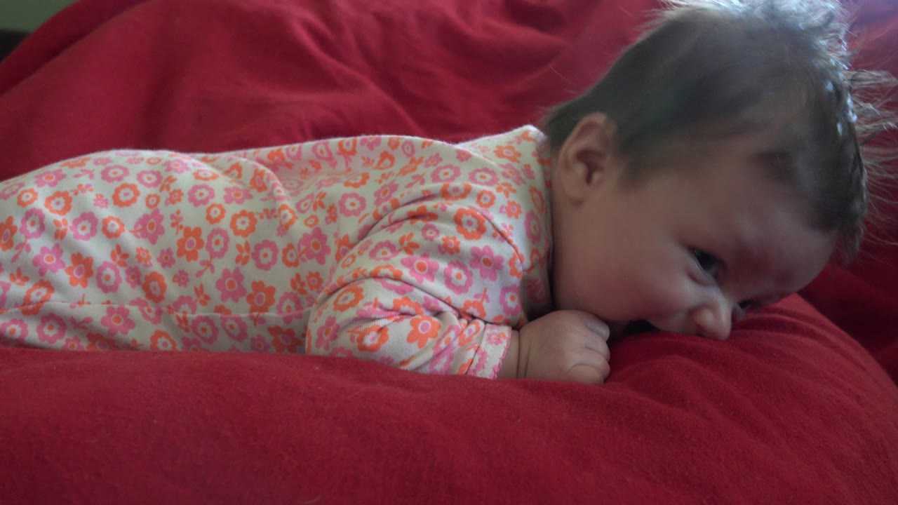 Baby lying face down on a red sofa
