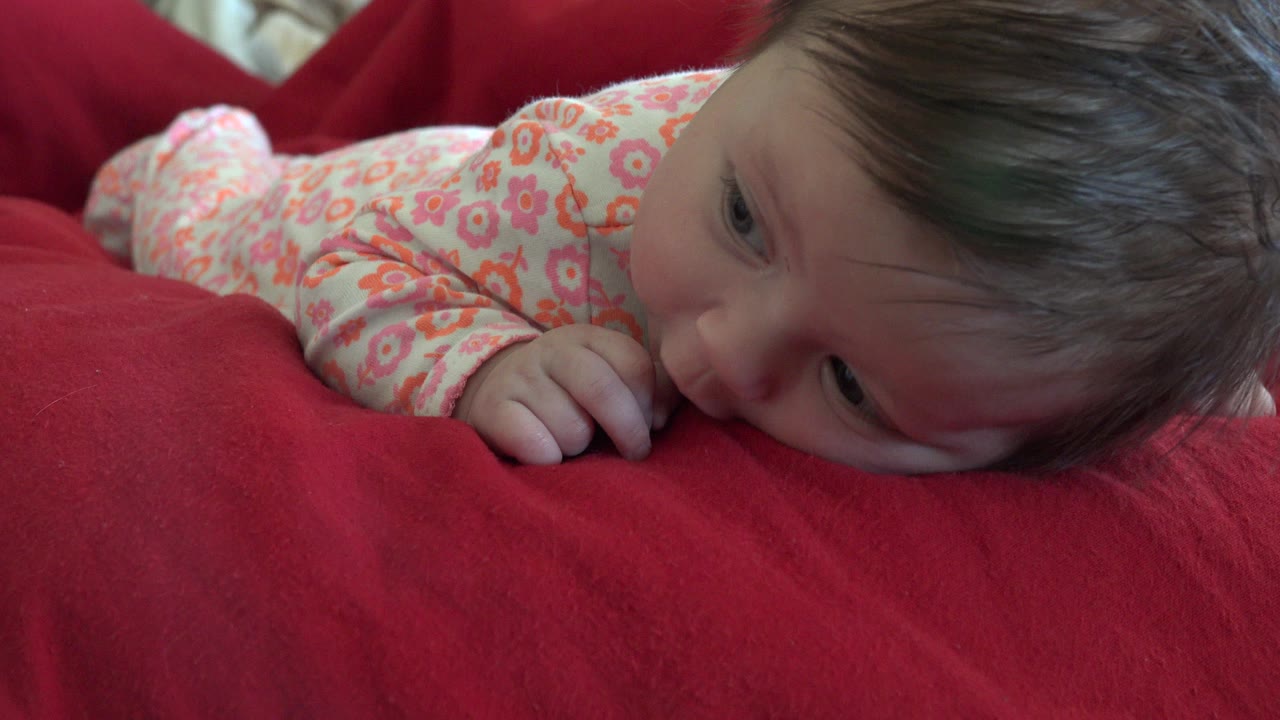 Baby lying on a red blanket in a floral onesie.