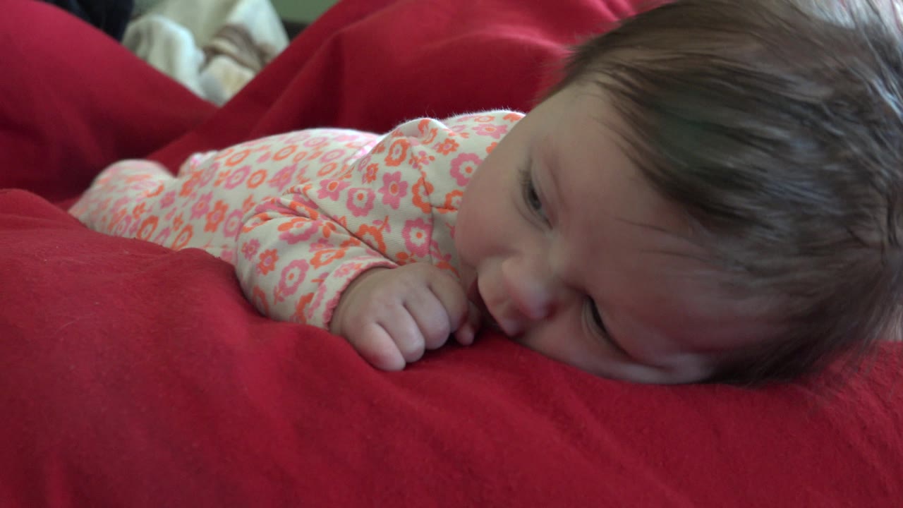 Baby lowering face toward the red blanket.