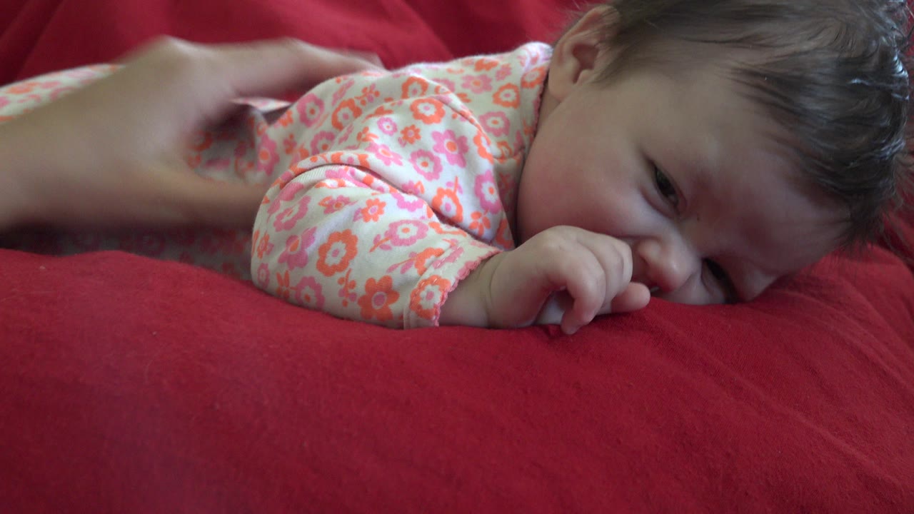At 0:00 in Westminster, Colorado 2015 footage, a young child in floral pajamas lies low on a red cushion with one eye partly visible.