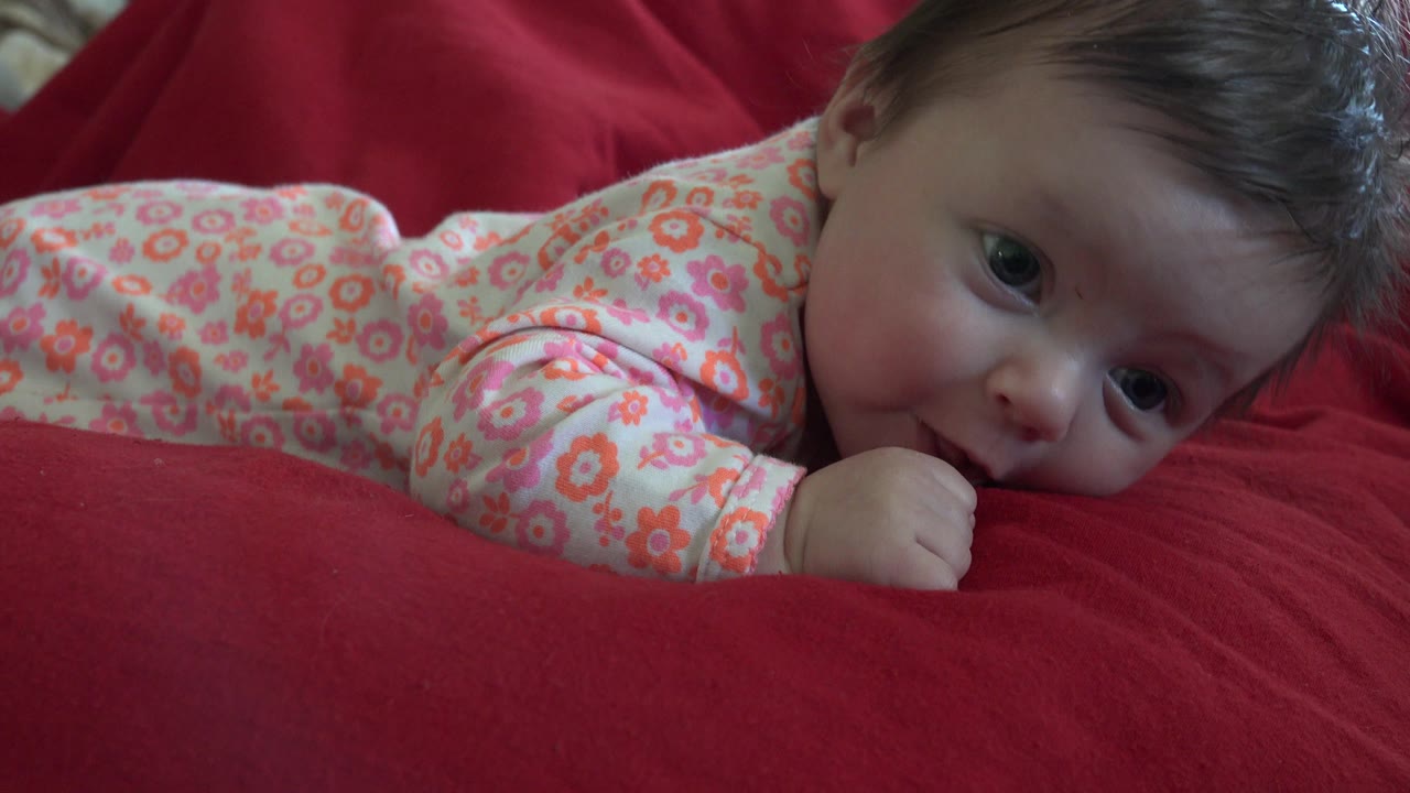 Baby looking toward the camera while lying on a red blanket.