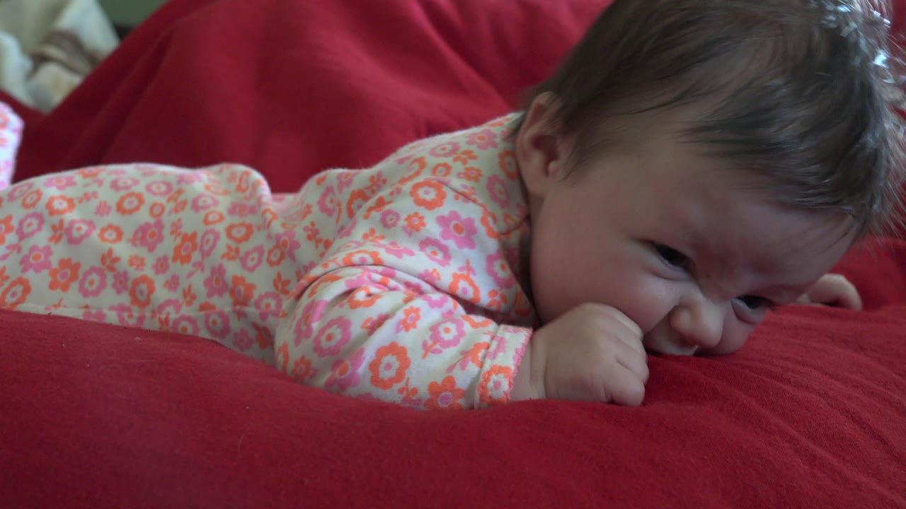 Infant lying face down on a red blanket.