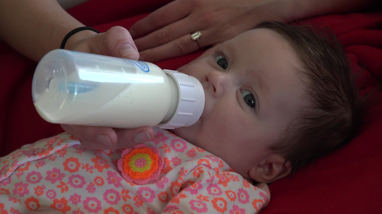 At 0:01 in Westminster, Colorado, the infant's eyes are open as the bottle rests at the mouth and the adult hand steadies it from the left side of frame.