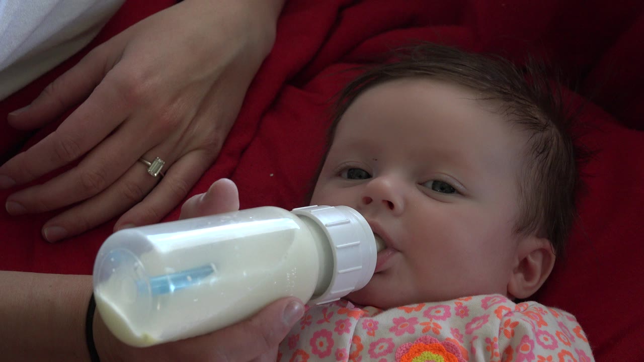 Baby drinking from a milk bottle on a red blanket.