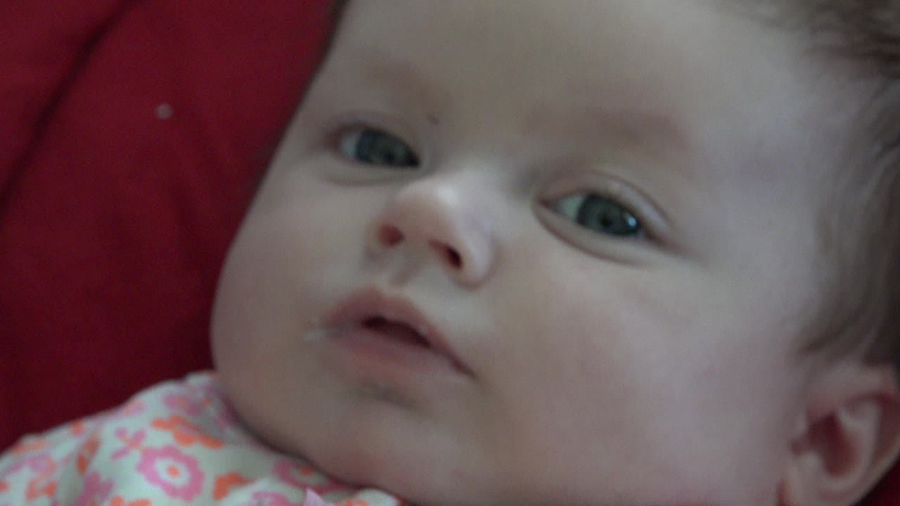 Baby lying on red fabric with eyes partly open.