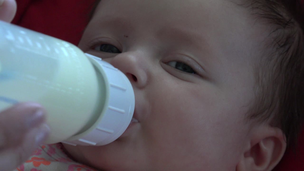 Newborn baby drinking from a milk bottle in close-up.