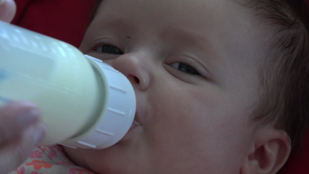The newborn's eyes are partly open as the bottle nipple rests at the mouth, with the bottle angled across the left side of the frame in Westminster, Colorado.