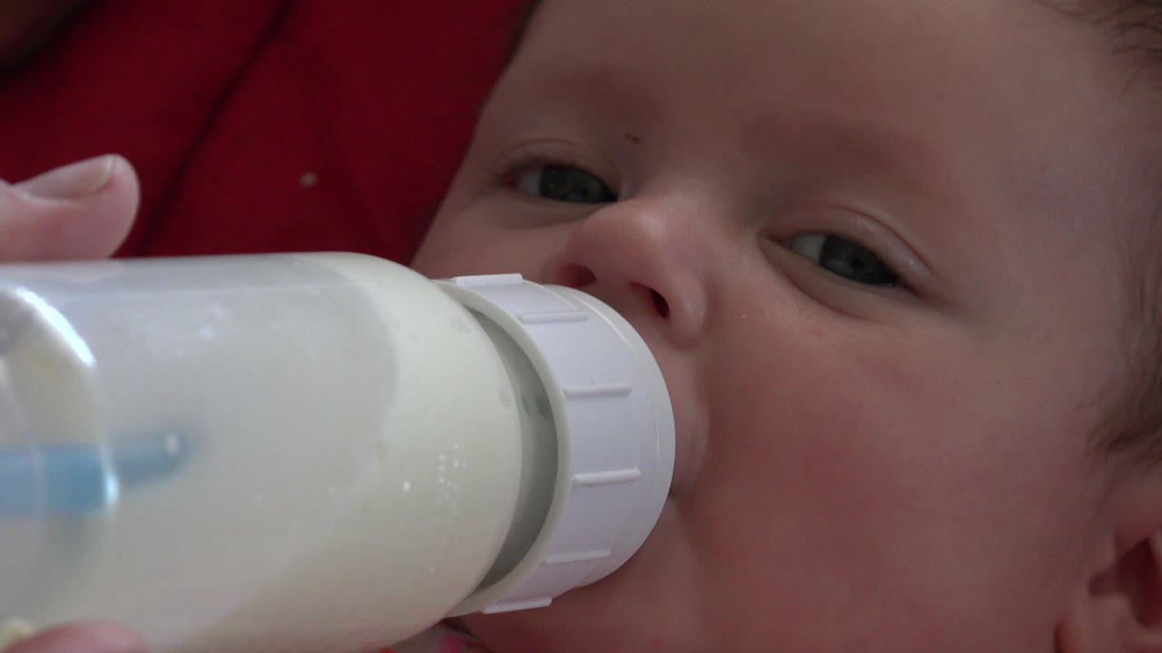 Newborn baby drinking milk from a bottle on red cloth.