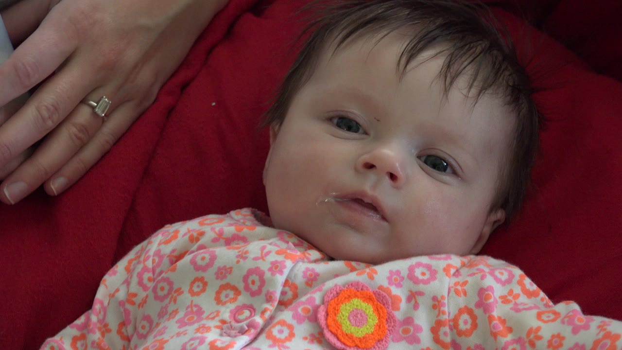Infant lying on red fabric with an adult hand nearby.
