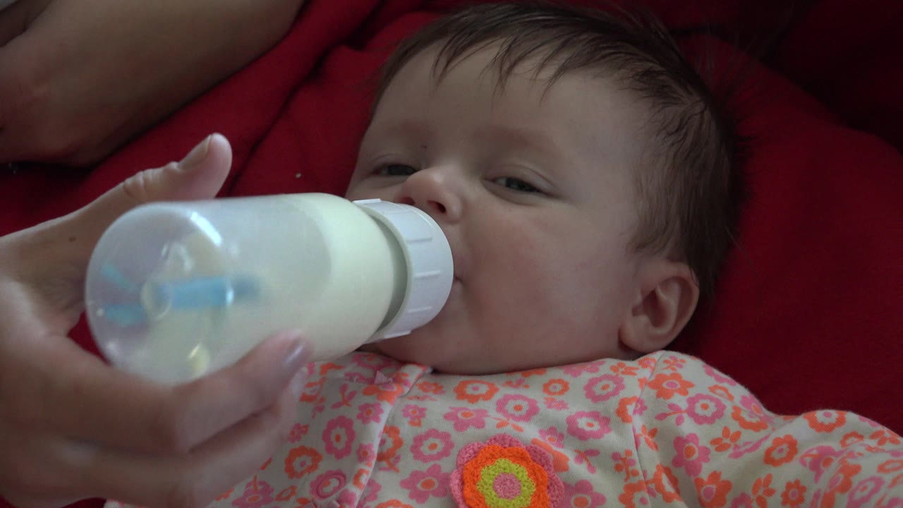 Infant drinking from a milk bottle on a red blanket.