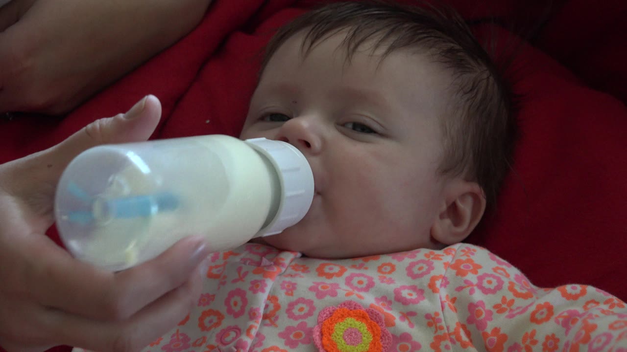 At 0:01, the baby's face remains partly behind the bottle as an adult hand steadies the milk bottle against the infant's mouth in the Westminster, Colorado clip.