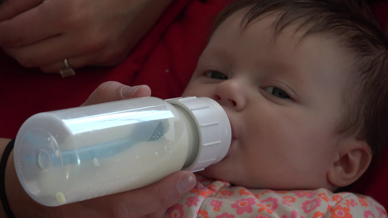 Baby drinking from a milk bottle on red fabric.