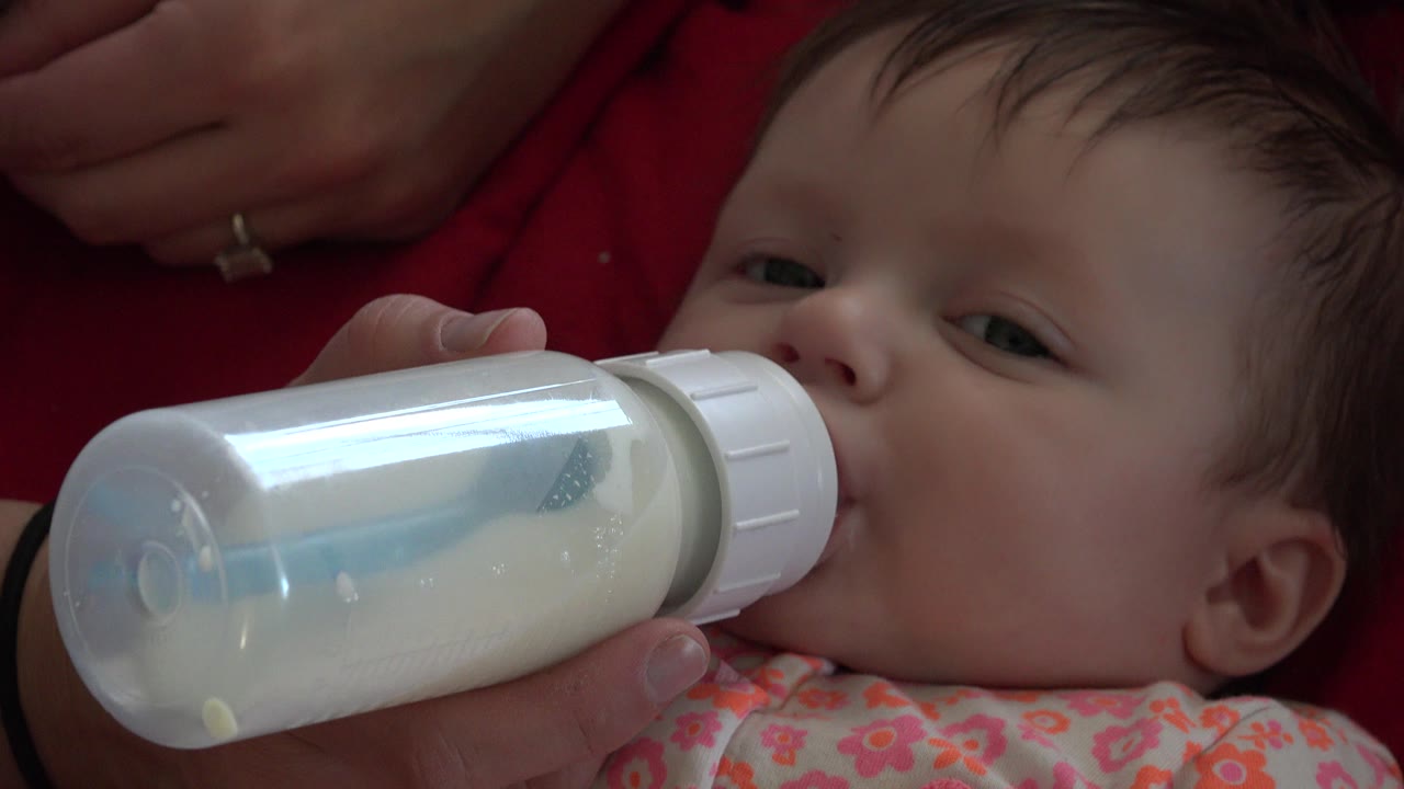 The baby's eyes remain partly open while the milk bottle rests at the mouth, with an adult hand steadying it in the Westminster, Colorado home-video frame.