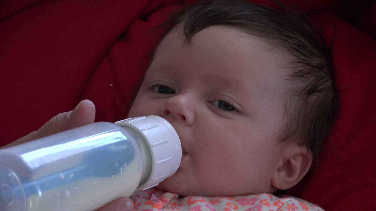 In Westminster, Colorado, a baby lies back on deep red padding while a translucent milk bottle rests against the mouth at the start of the clip.