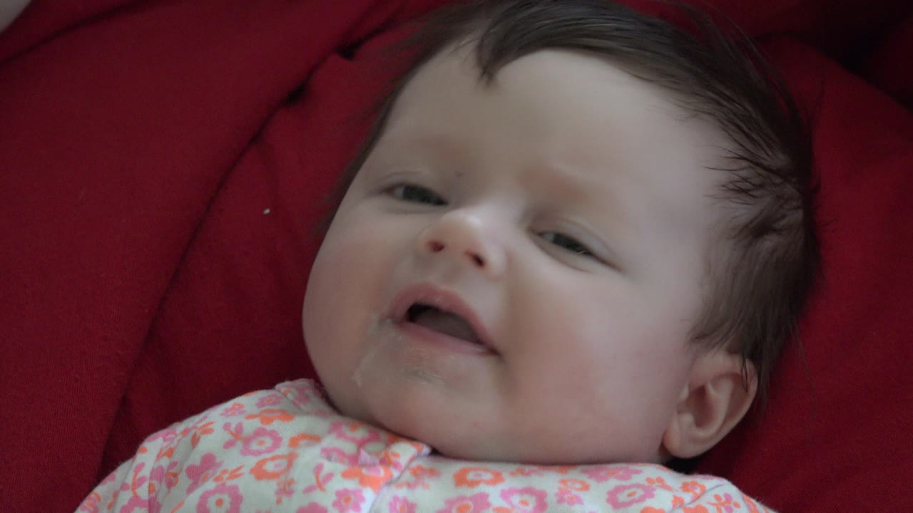 Baby lying on red cushion and looking toward the camera.