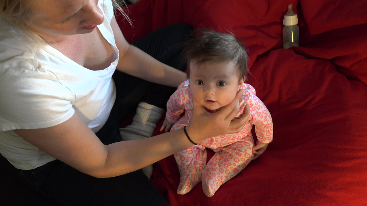 Woman steadies a baby sitting on a red couch.