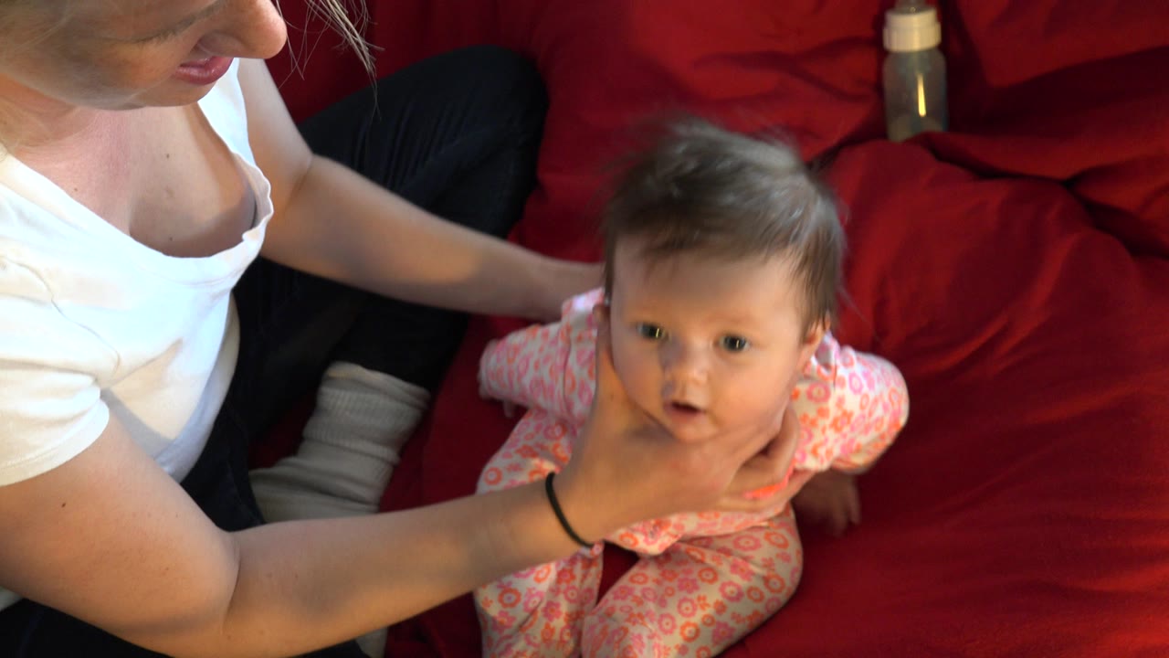 Woman supports a baby sitting on a red bedspread.