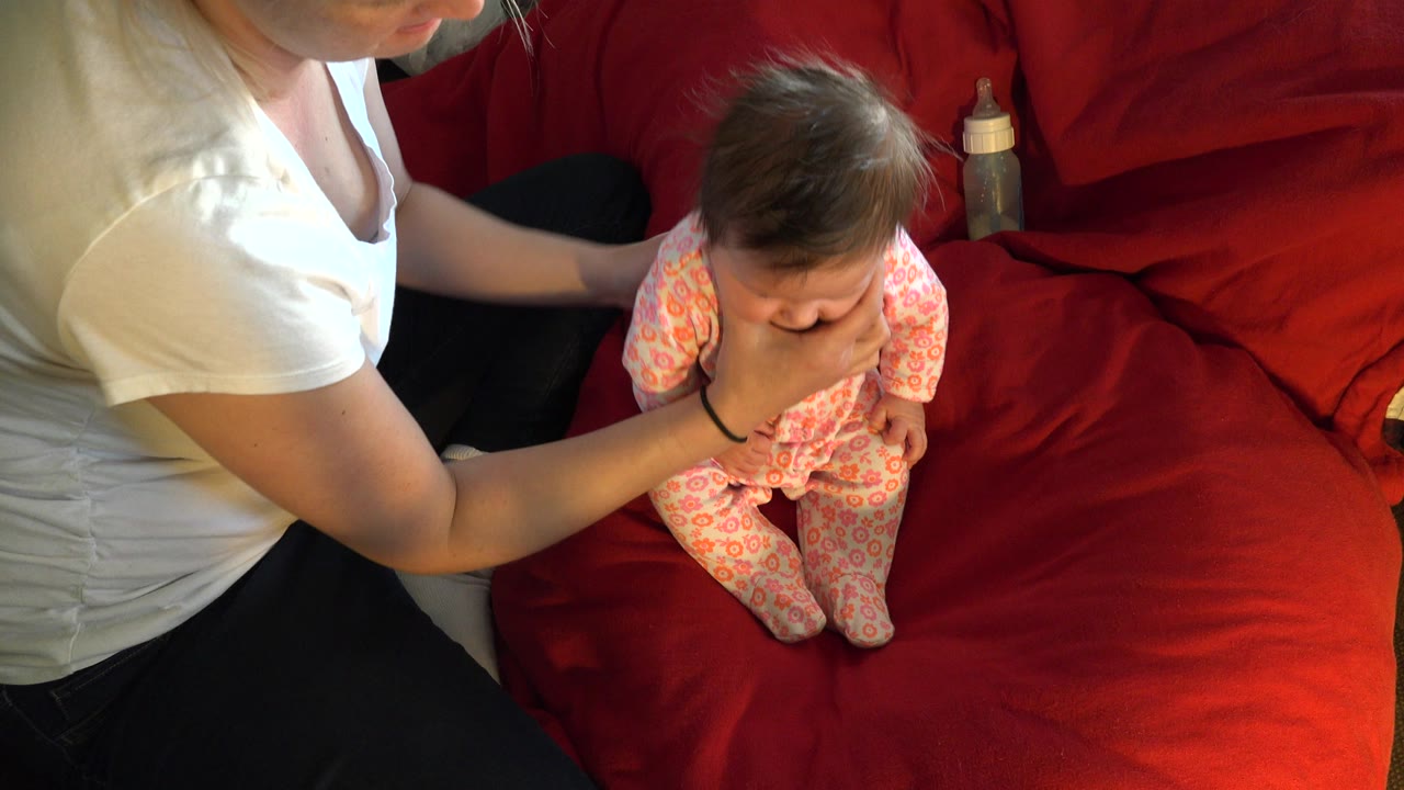 Mother holding a baby upright on a red couch.