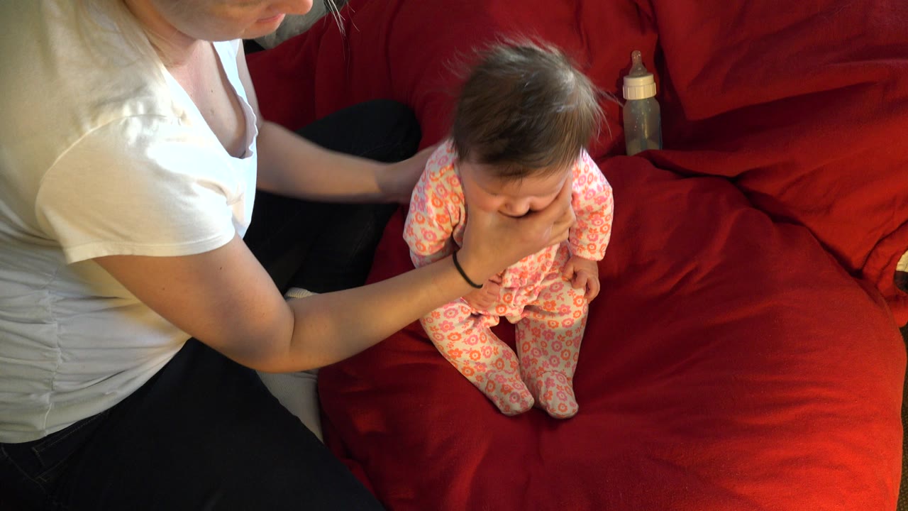 One second in, the baby faces downward while the mother keeps a hand at the baby's chest on the red couch in Westminster, Colorado.