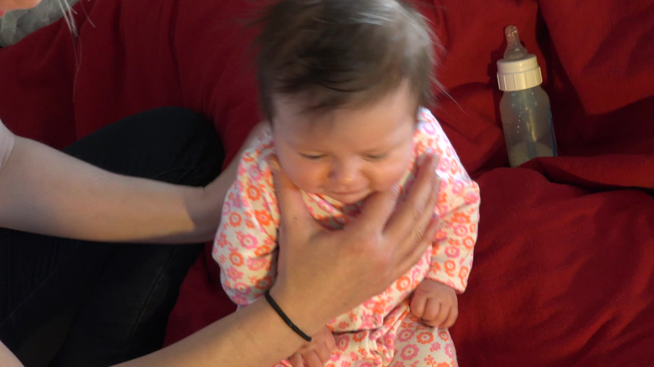 Baby leaning forward as an adult hand supports the chin and chest.