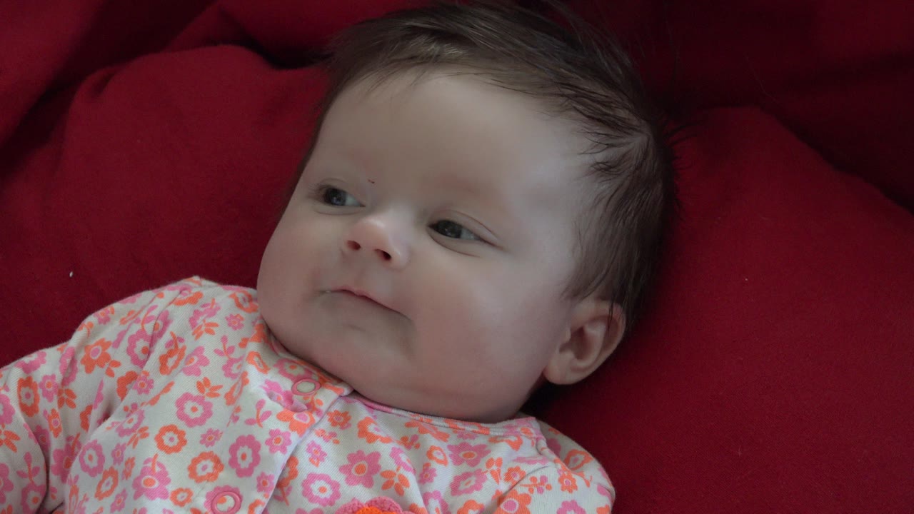 Baby lying on red bedding and looking off to the side.