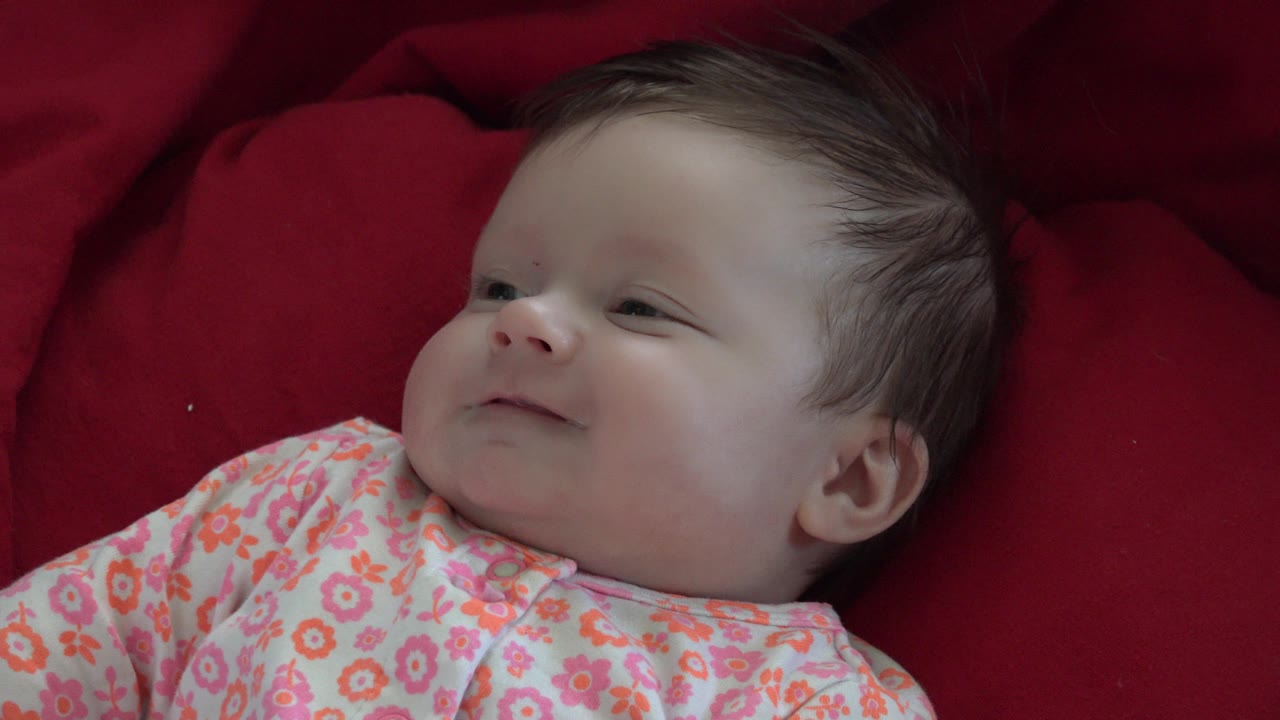 A close view shows the baby in Westminster, Colorado resting against the red blanket with a gentler expression and the floral outfit visible across the foreground.
