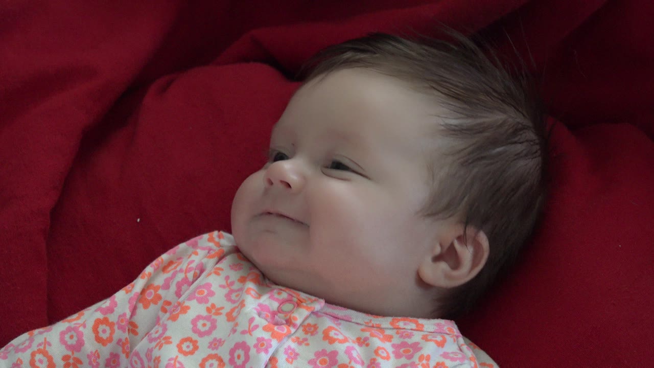 Baby in floral pajamas lying on a red blanket and looking to the side.