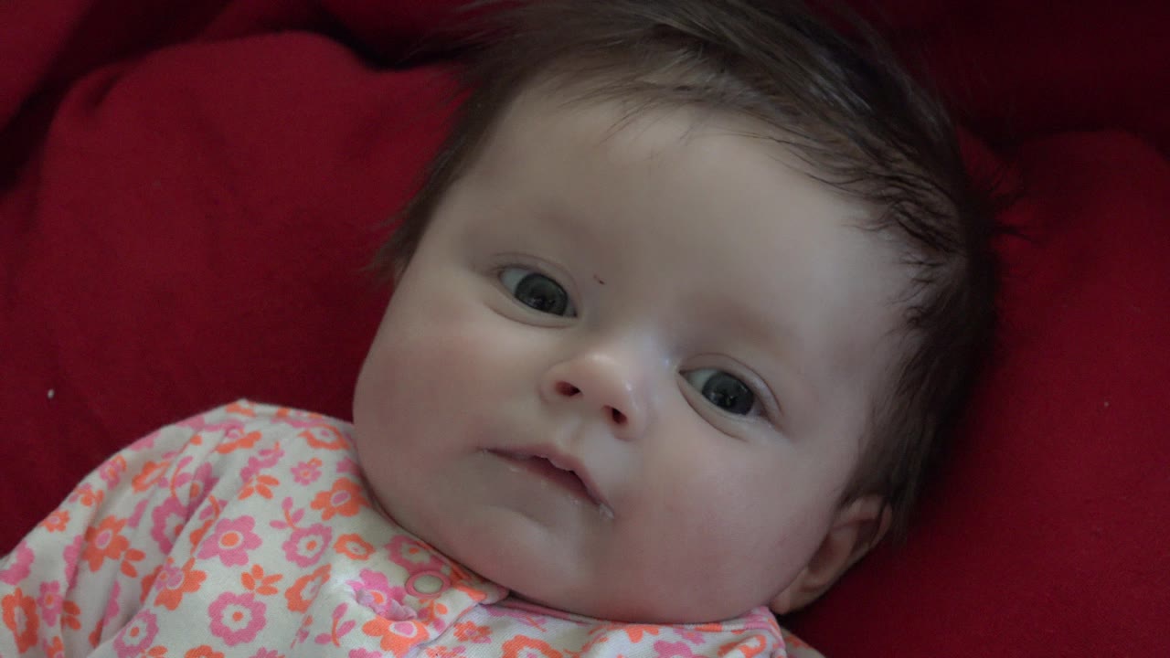 Baby lying on a red blanket in flowery clothes.