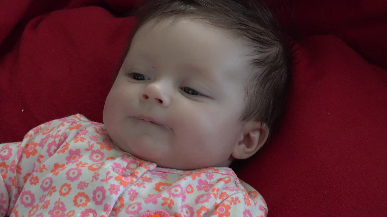 Baby lying on a red cushion in a floral onesie.