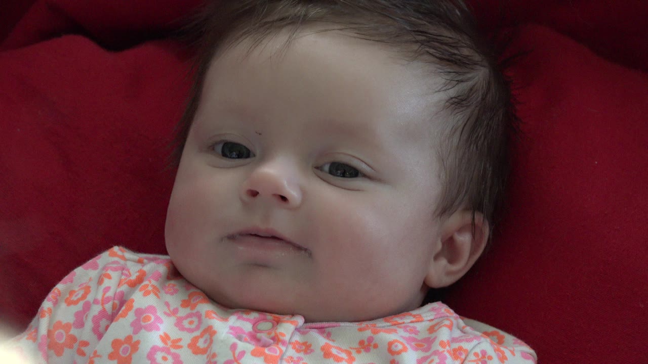 Baby lying on red bedding in a floral outfit.