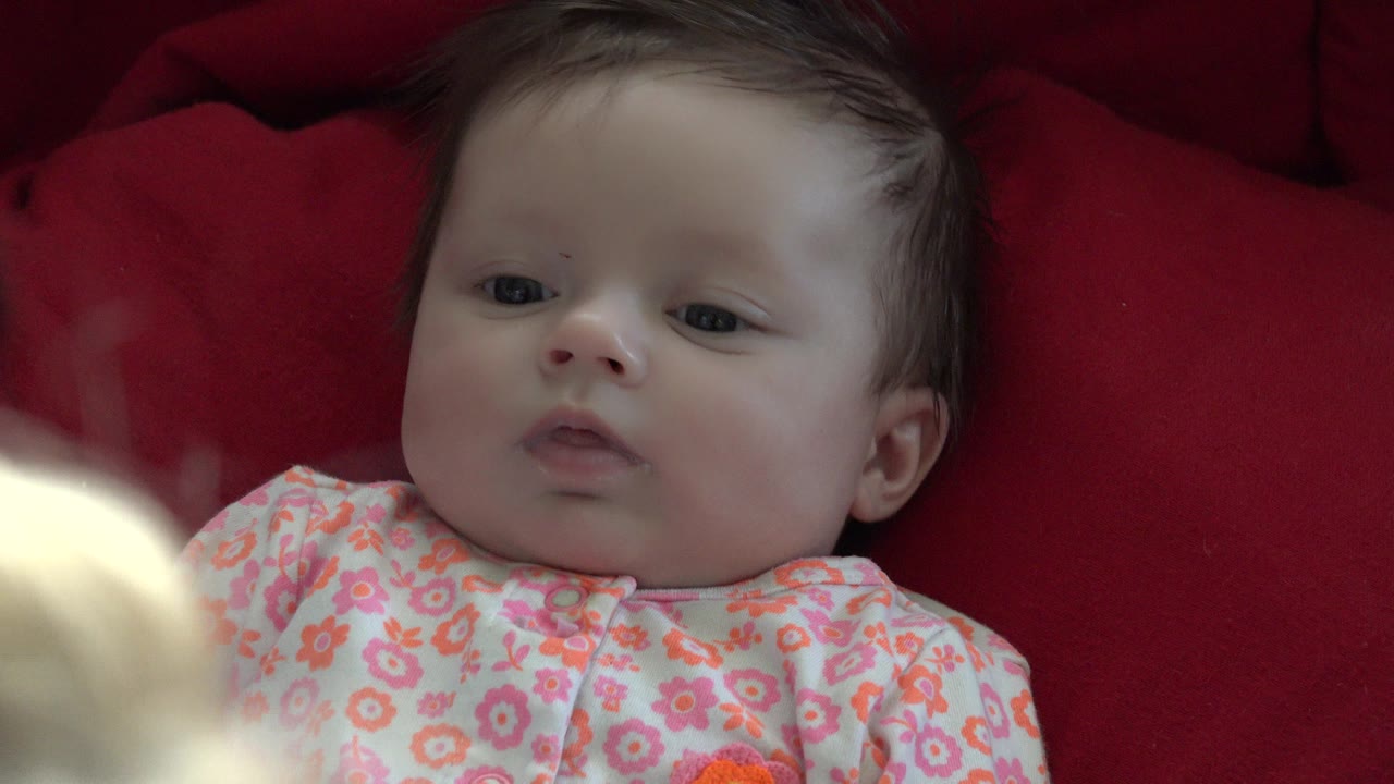 Baby lying on red fabric in a floral outfit.