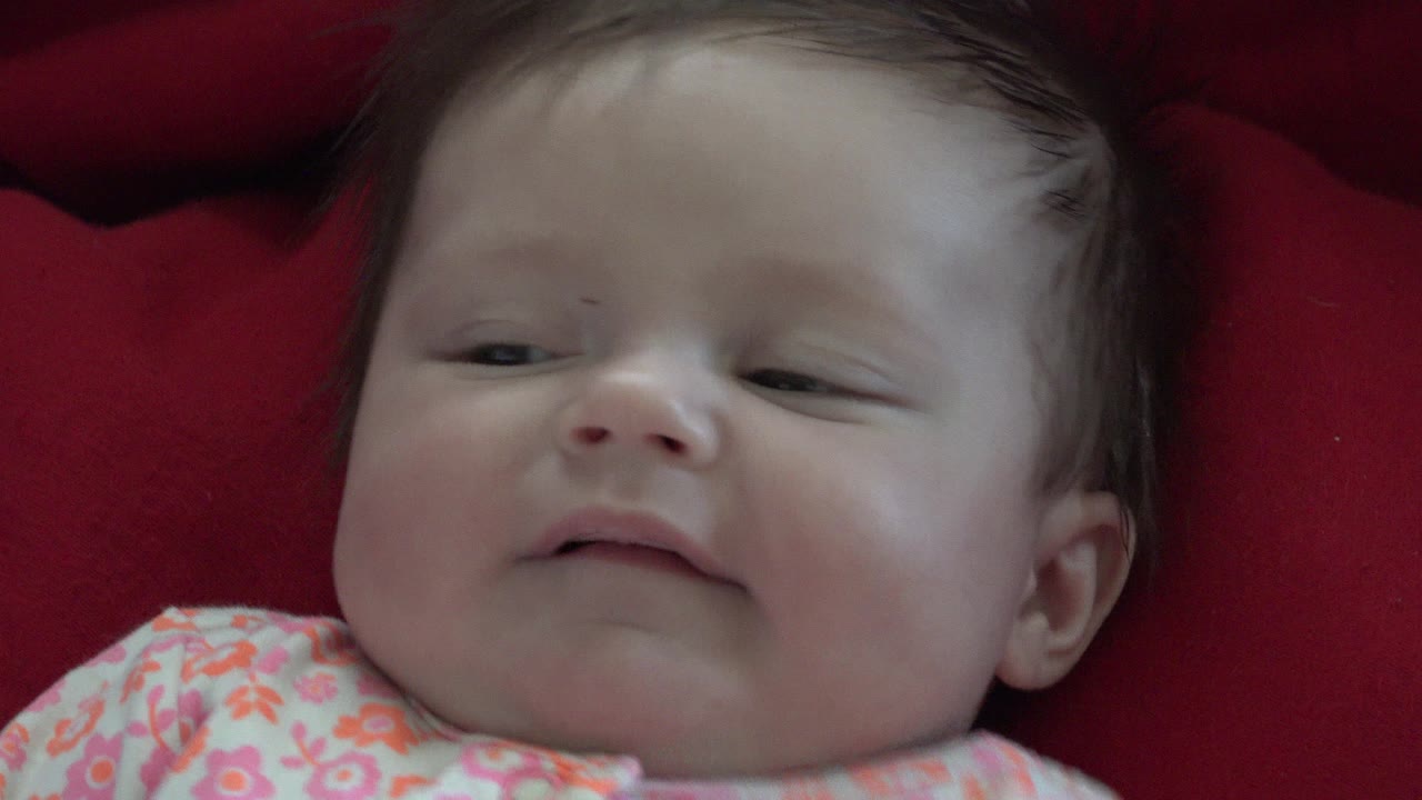 Newborn baby lying on a red blanket in a floral outfit.