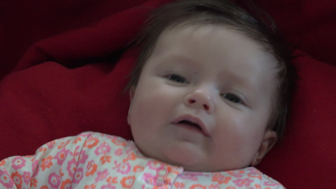 Baby lying on red fabric in a floral outfit.