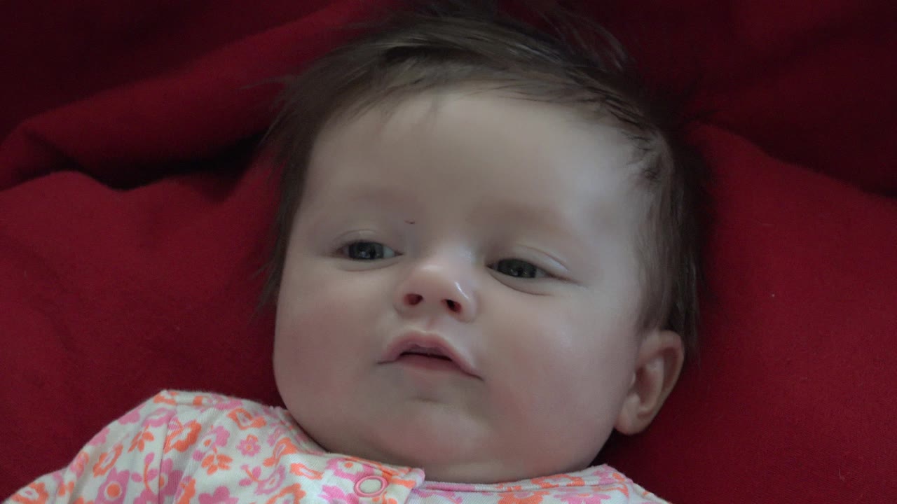 Baby lying on red fabric with a neutral expression.