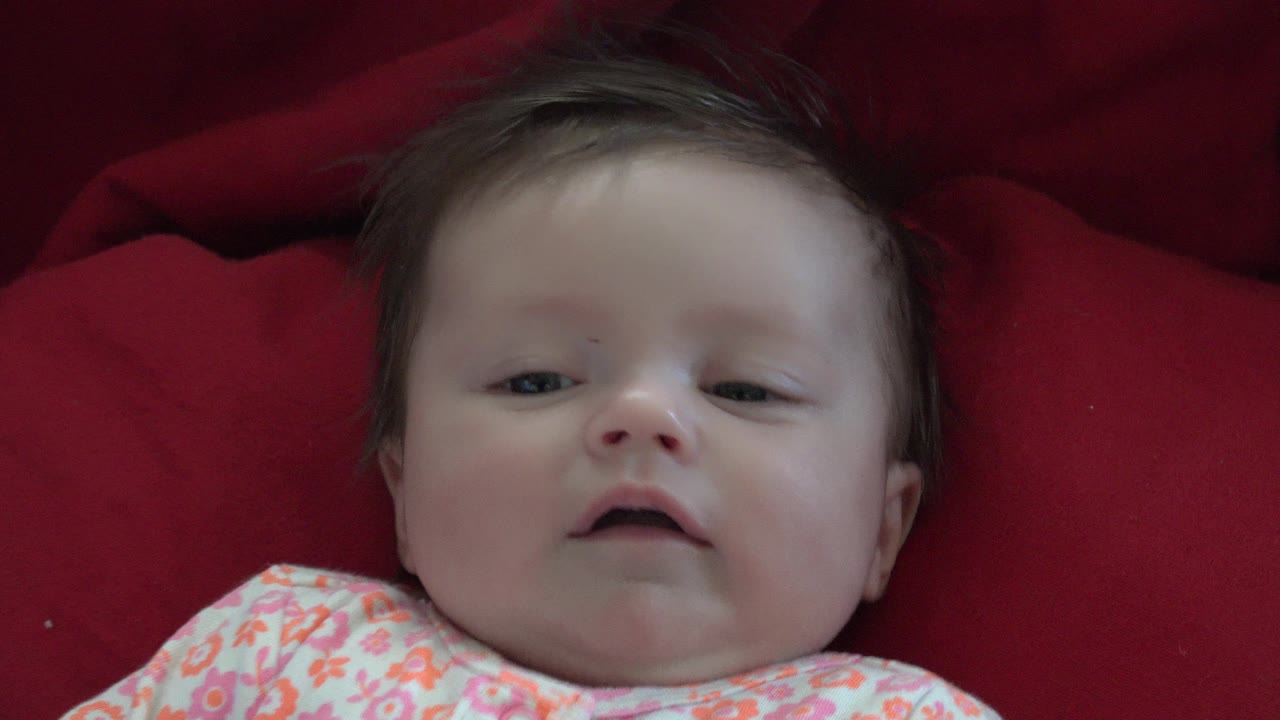 Baby lying on red bedding in a floral outfit.