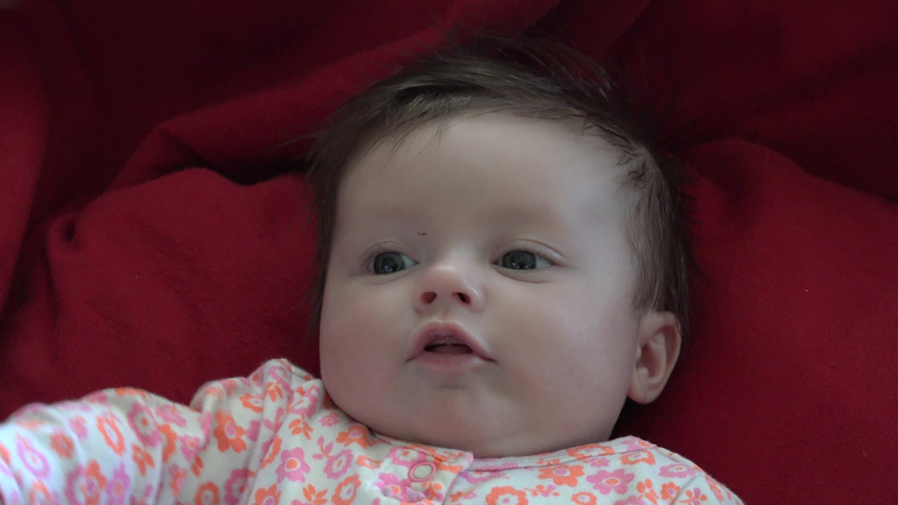 Infant on red cushions with an arm entering the lower frame.