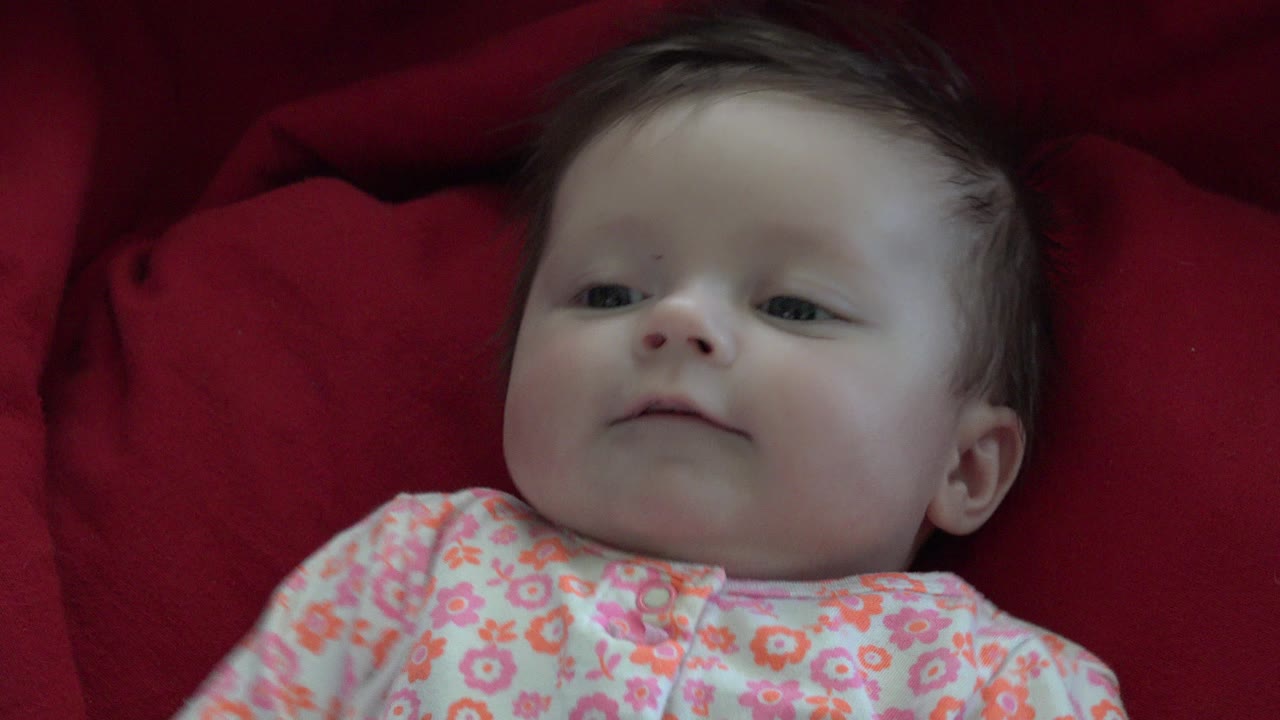 Infant lying on red fabric in a floral onesie.